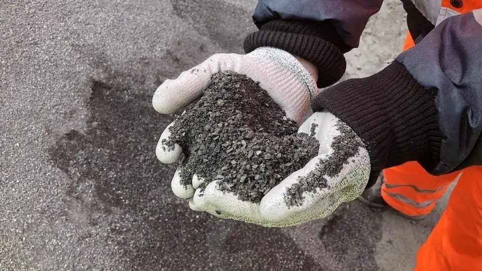 Gloved hands holding a handful of crushed grey rock.